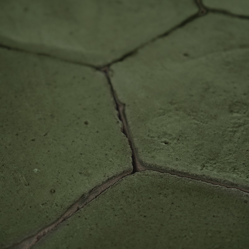 Azulejo verde hexagonal com fissuras visíveis e rejunte escuro; superfície gasta e irregular, placas adjacentes formando padrão contínuo.