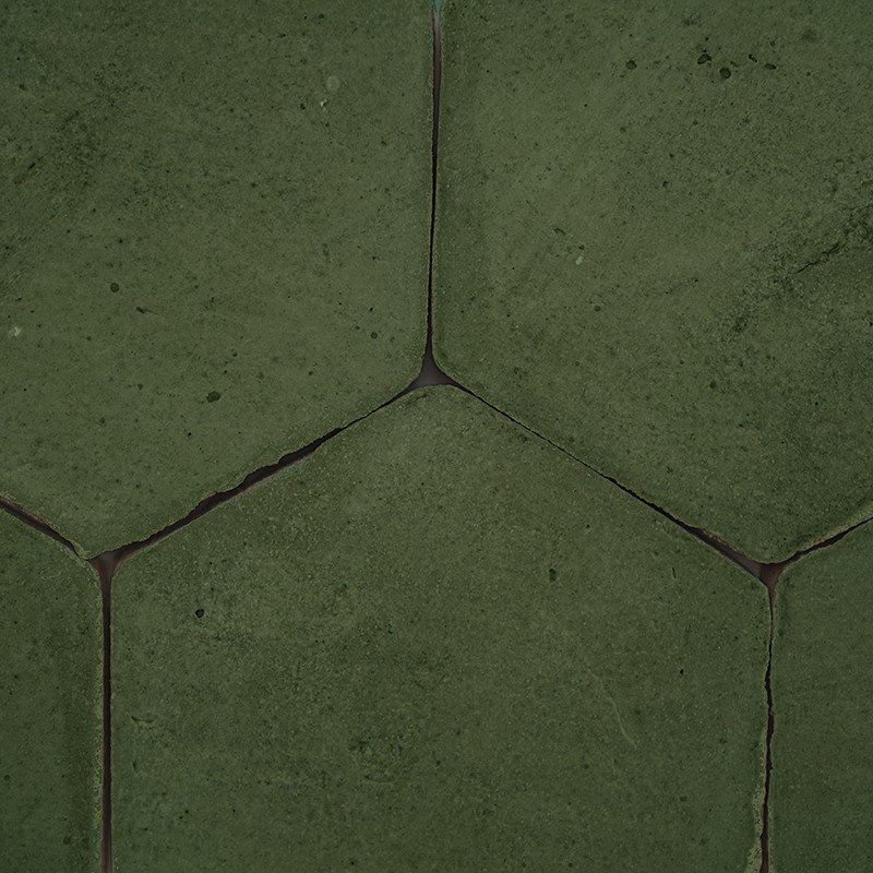 Dark green hexagonal tile, matte surface with small porosities and wear; narrow, dark joints forming triangular intersections between the pieces, repeated arrangement.