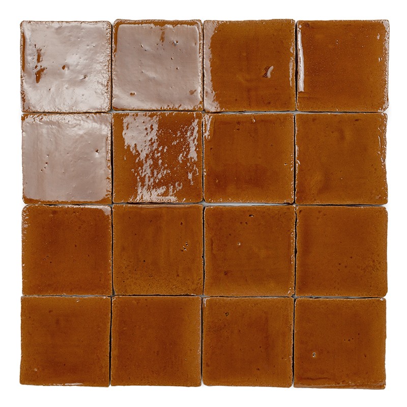 Carrelage 4x4 de petits carreaux céramique brun-ambre brillants, nuances et reflets irréguliers, joints fins crème, surfaces légèrement ondulées et ébréchures visibles.