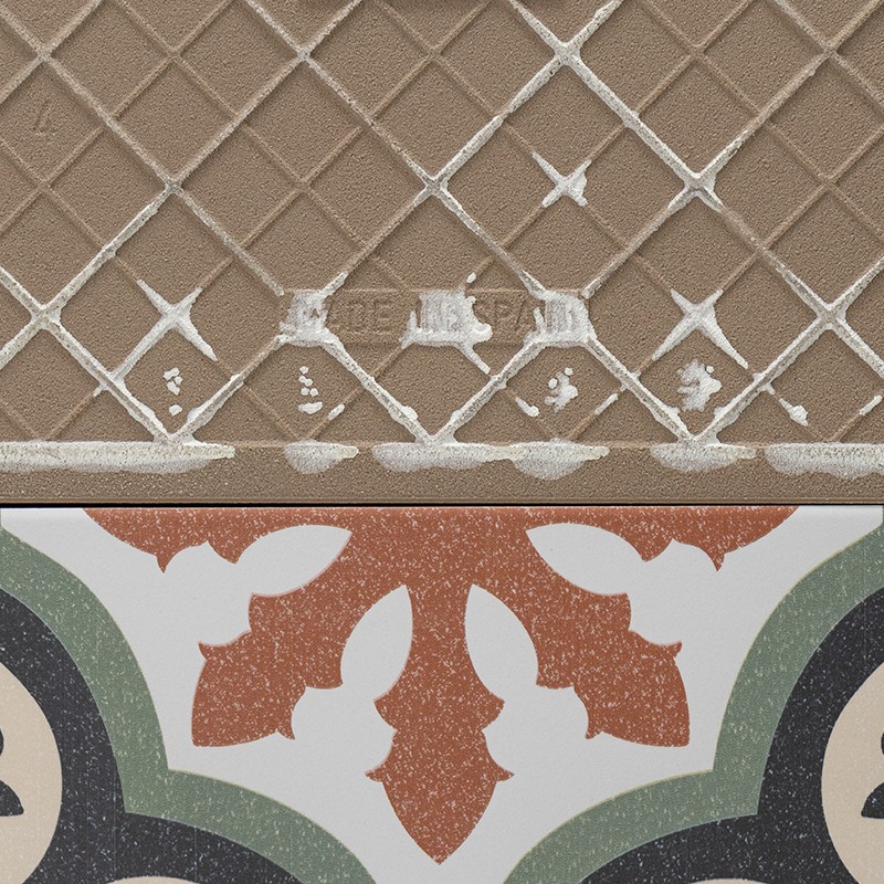 Carrelage losangé beige à relief blanc, bord supérieur usé; bande inférieure d'un carreau décoratif multicolore (vert, noir, brique).   Texte : traces de lettres blanches illisibles dans les losanges.