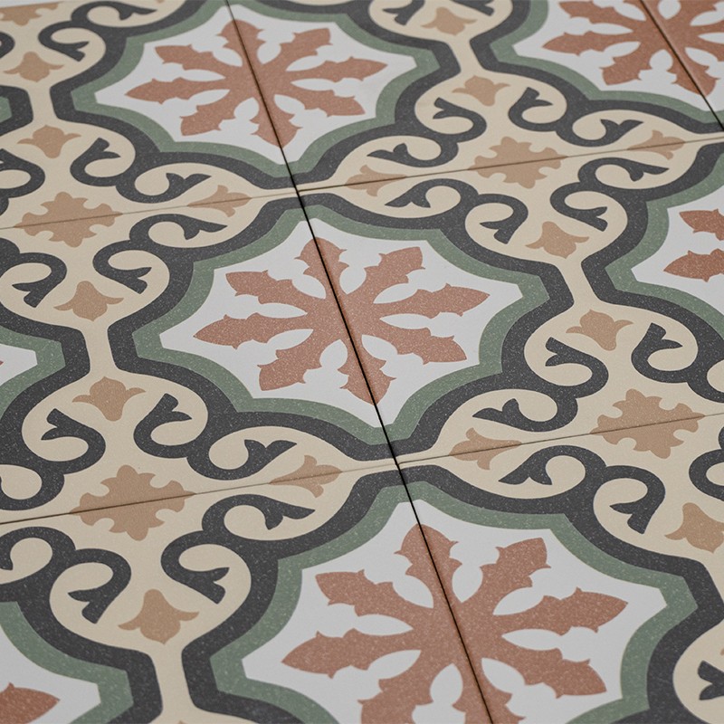 Carrelage décoratif au sol à motifs géométriques répétitifs : fleurs stylisées ocre sur fond blanc, bordures vertes et arabesques gris foncé; joints visibles formant lignes droites.