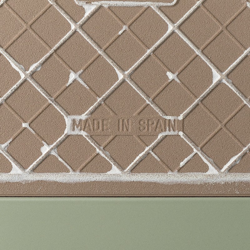Azulejo texturizado color beige con patrón romboidal en relieve, inscripción central: MADE IN SPAIN; borde inferior liso color verde.