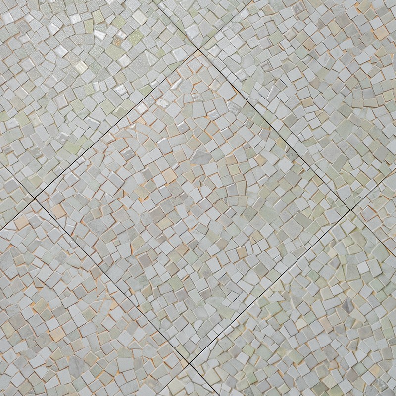 Carrelage en petits carreaux mosaïque crème et beige, formant des motifs irréguliers au sein de grands carrés délimités par joints gris, vue en plongée.