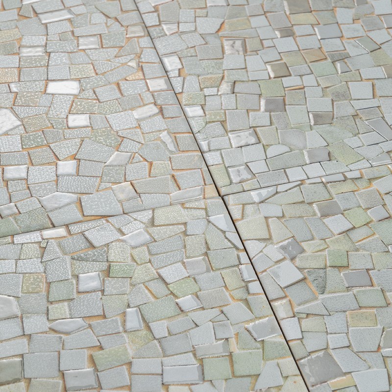 Carrelage mosaïque de petits carreaux irréguliers ivoire, beige et vert pâle, joints ocres, avec une rainure centrale marquant la séparation de deux dalles, surface plane.