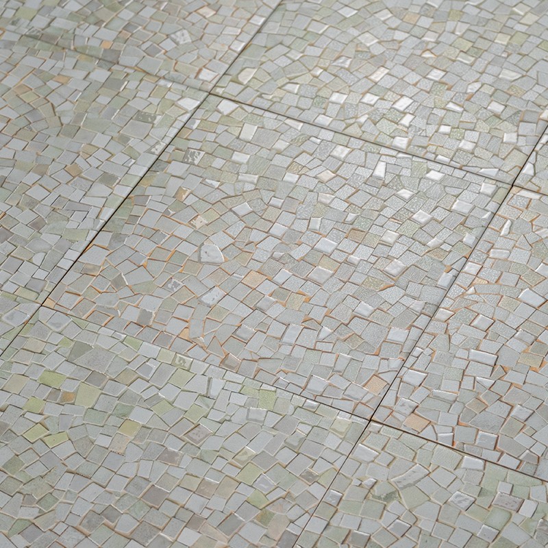 Mosaic tile of small irregular fragments cream and beige; several tiles forming a floor with visible joints.