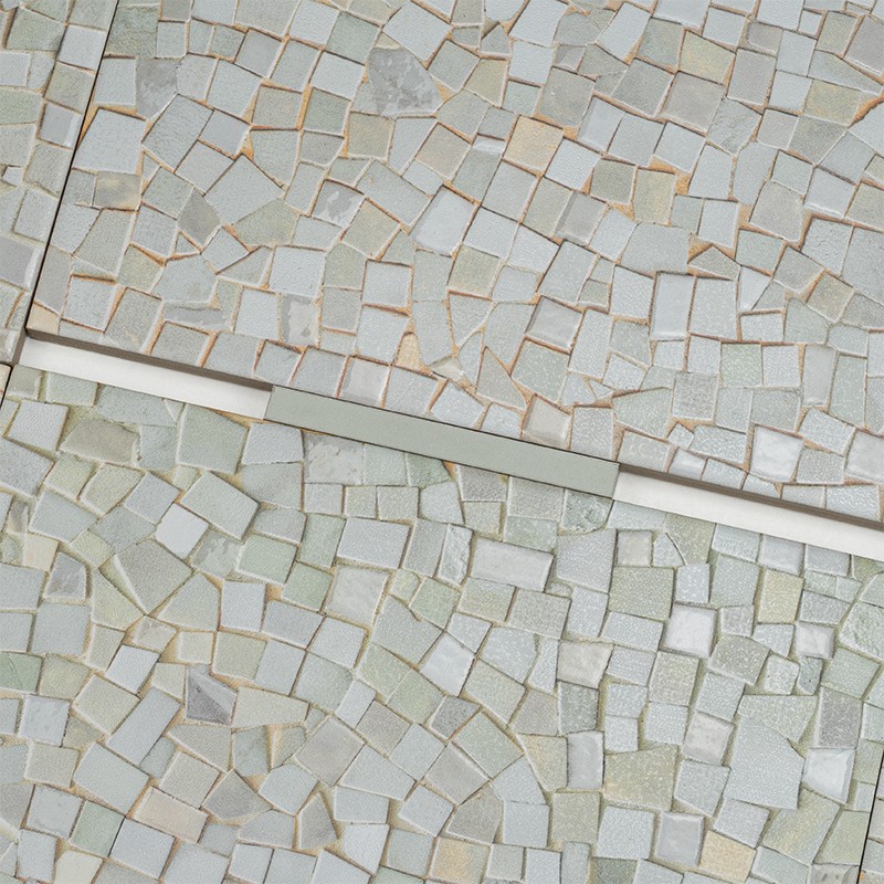 Azulejo mosaico de pequeñas piezas irregulares blanco crema; un listón blanco divide dos secciones similares, juntas visibles y textura ligeramente rugosa.