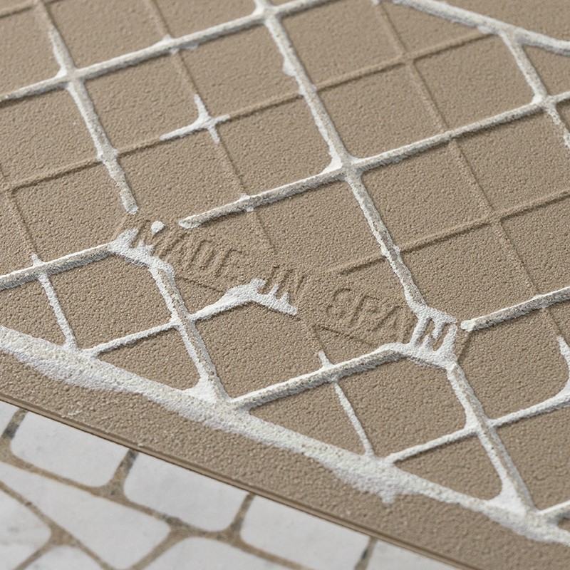 Beige Fliese mit erhabenen quadratischen Feldern und weißer Fugenmasse; eingedrückter, teilweise lesbarer Schriftzug: "…SKIN".