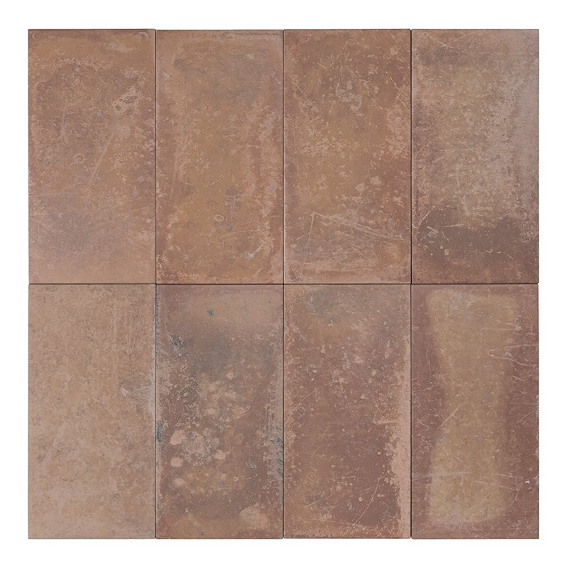 Azulejo rectangular marrón rojizo con textura desgastada y motas claras, borde ligeramente erosionado; fondo blanco sugiere presentación aislada sobre superficie neutra.