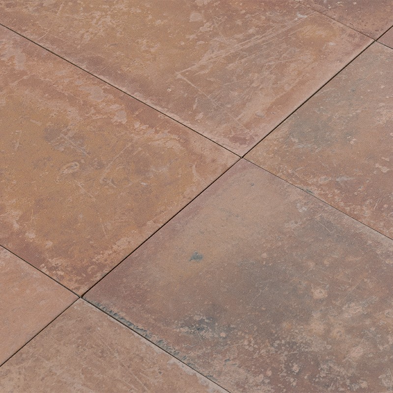 Carrelage carré brun-beige, coins se rejoignant en croix, surface usée et tachée, variations de teinte et dépôts de saleté, semblant être un sol extérieur ou une terrasse.