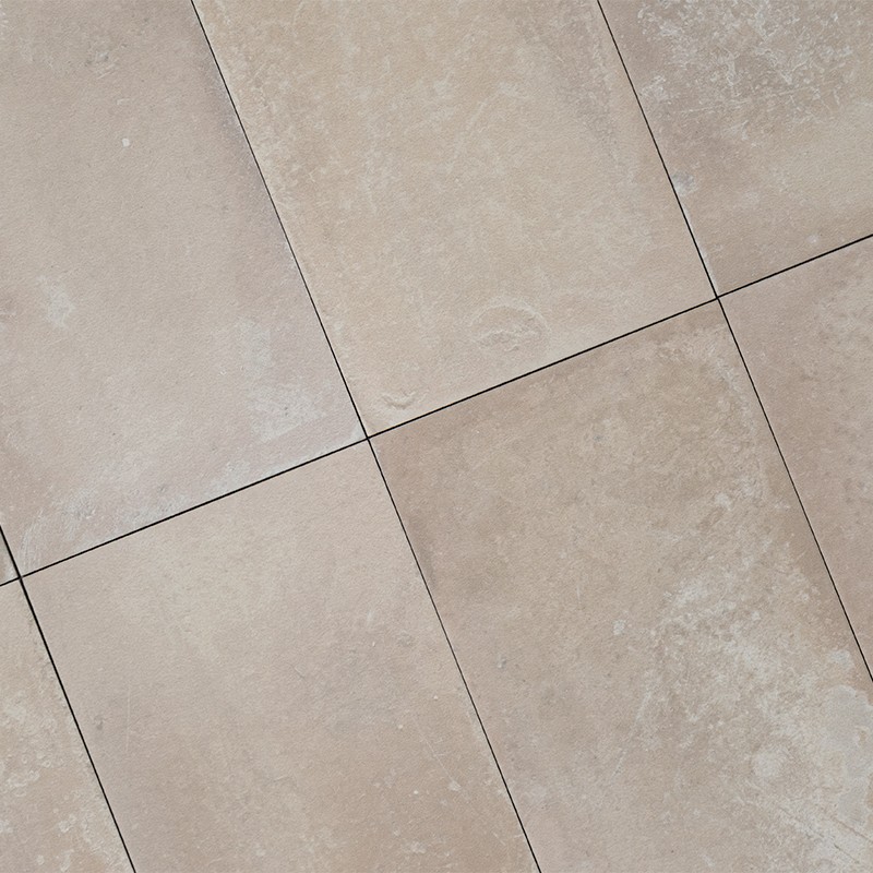 Azulejos cerâmicos quadrados bege claro com discreta marmorização; juntas finas escuras formam grade diagonal; superfície texturizada e fosca, aparentando piso interior.