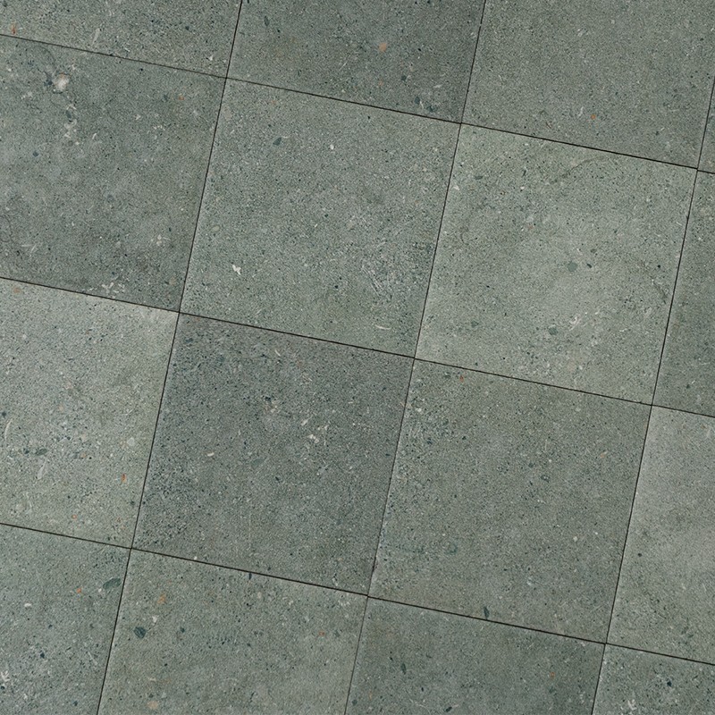 Azulejos cuadrados de piedra gris verdosa con textura moteada; colocados en cuadrícula regular con juntas finas, formando un pavimento o revestimiento interior.