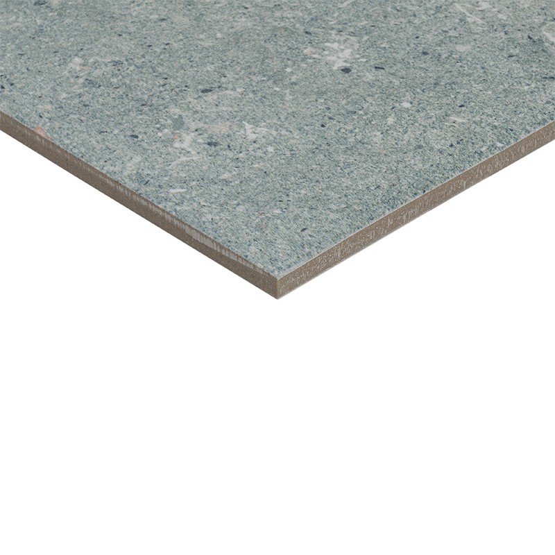 Azulejo retangular azul-acinzentado com padrão marmorizado; borda exposta revela núcleo marrom, apoiado sobre fundo branco.