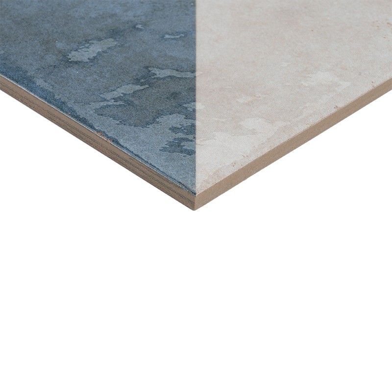Tegel met diagonale tweekleurige afwerking: linkerhelft blauwgrijs met vlekkerig patroon, rechterhelft lichtbeige; dunne zijkantlaag zichtbaar tegen witte achtergrond.