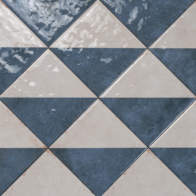 Carrelage de carreaux triangulaires alternant bleu foncé et crème formant motif en losanges; surface brillante avec reflets et joints fins, sol intérieur apparent légèrement usé.