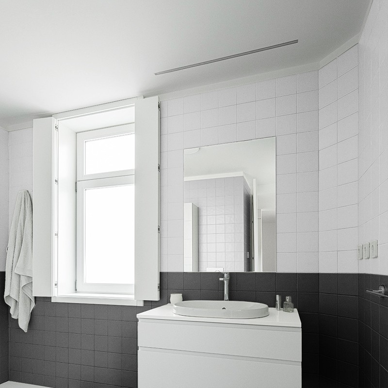 Tegelwand, donkergrijs onder en lichtgrijs boven, in moderne badkamer met witte wastafelkast, ronde waskom, spiegel, raam met luiken en handdoek links.