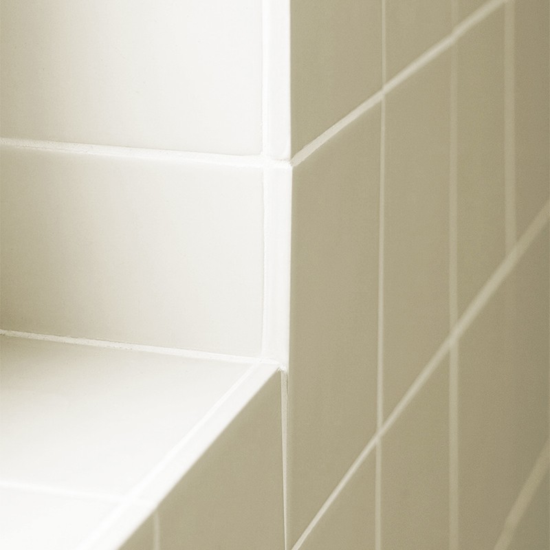 Carrelage crème lisse en angle, coin formant un rebord d'étagère carrelé, joints réguliers et lumière douce créant ombres et reliefs subtils.