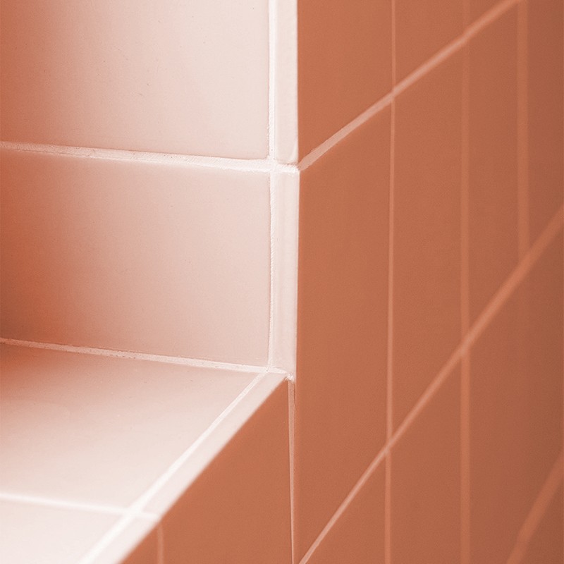 Pale pink rectangular corner shelf tile, with white joints and clean cut; surrounded by a wall of similar tiles arranged in a grid.