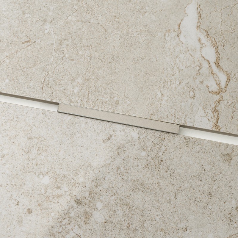 Beige tile with marbled veins; narrow, horizontal metal profile crosses the joint, on a polished surface of cream and light brown tones.