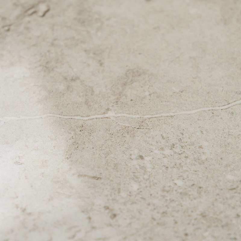 Azulejo creme marmorizado com fissura fina horizontal; superfície opaca, manchas de desgaste e sujeira leve, provavelmente piso ou revestimento de parede interno.