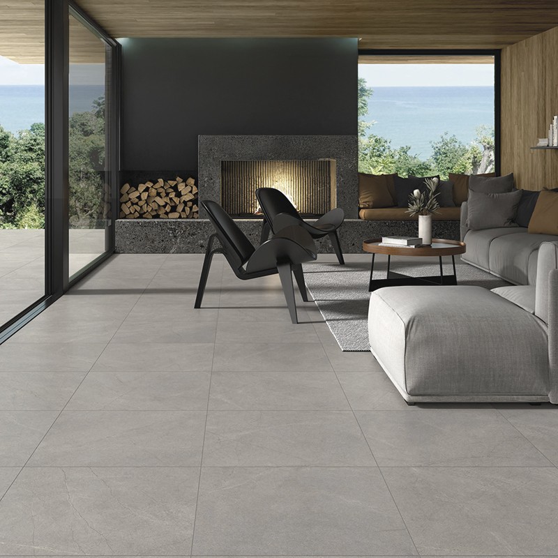 Große matte graue Bodenfliesen (Objekt) in modernem Wohnzimmer (Kontext) mit Kamin, Holzdecke, Sofalandschaft, schwarzem Lounge-Sessel und bodentiefer Glasfront mit Meerblick.