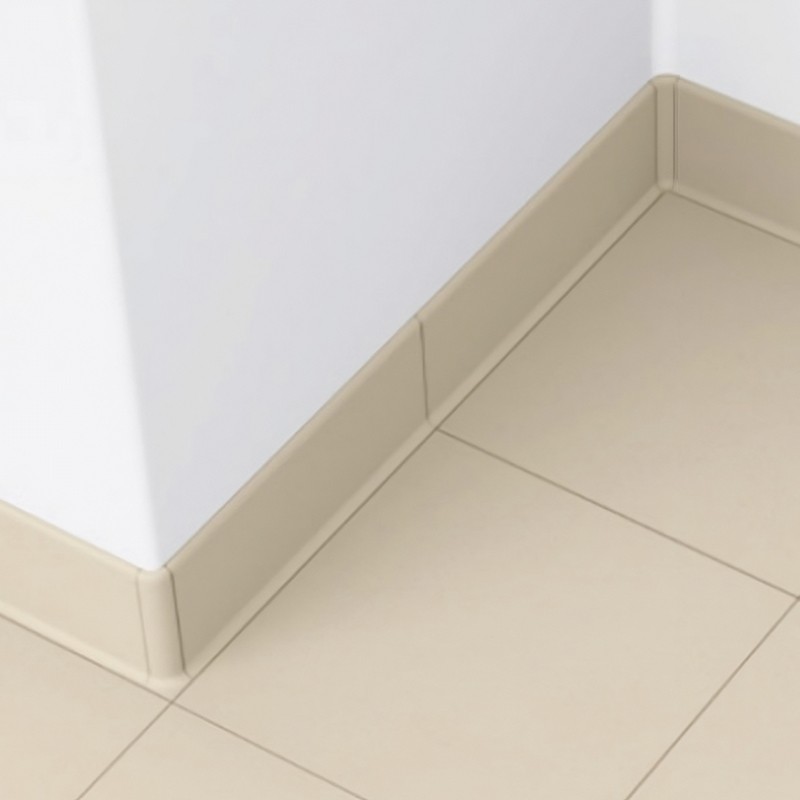 Carrelage beige mat à grands carreaux, au coin d'un mur blanc, avec plinthe beige assortie et joints fins, formant un angle intérieur net.