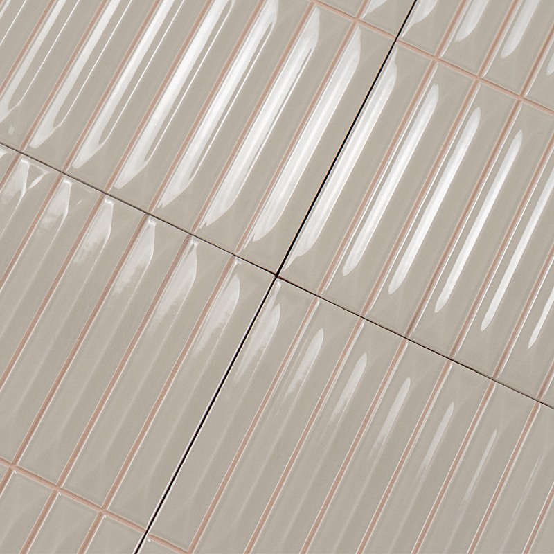 Carrelage mural beige brillant: carreaux rectangulaires étroits verticaux à nervure centrale, joints fins rosés; fine fissure noire traverse une jonction diagonale entre quatre carreaux.