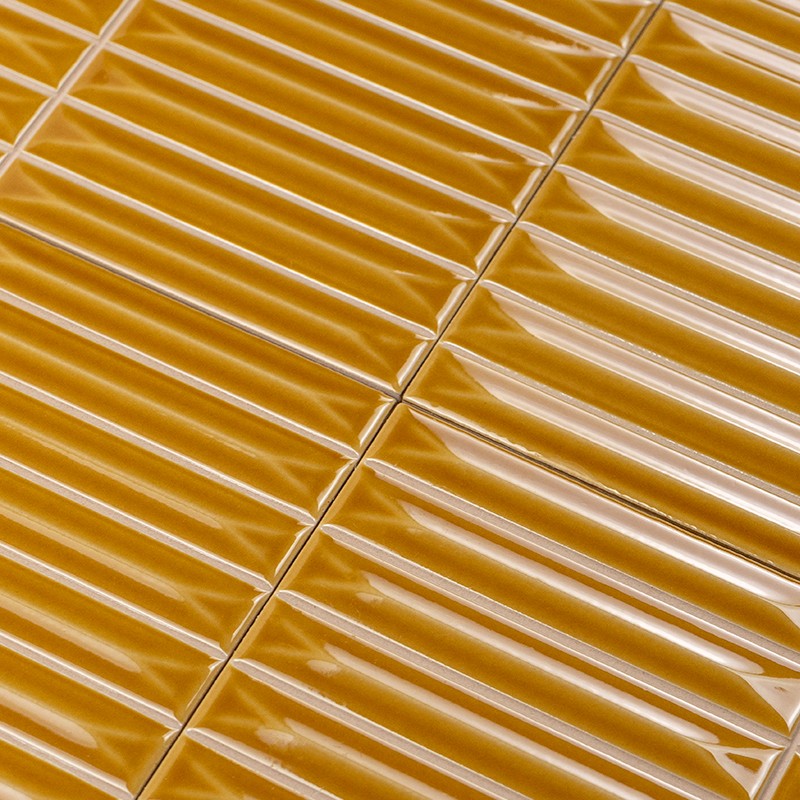 Carrelage rectangulaire jaune moutarde, reliefs et reflets brillants légèrement ondulés; joints fins blancs créent une trame régulière, deux lés de carreaux se rejoignent en diagonale.