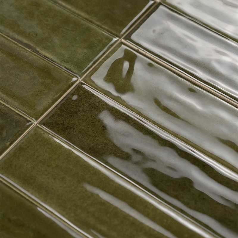 Donkergroene, geglazuurde, rechthoekige tegels met zichtbare voegen en glanzende reflecties, geplaatst in een regelmatig raster; sommige tegels tonen licht golvend oppervlak.