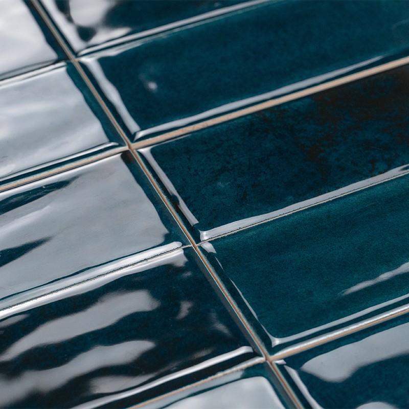 Azulejos rectangulares esmaltados color azul oscuro verdoso, brillo reflectante; juntas estrechas y claras formando una cuadrícula, superficie ligeramente ondulada.