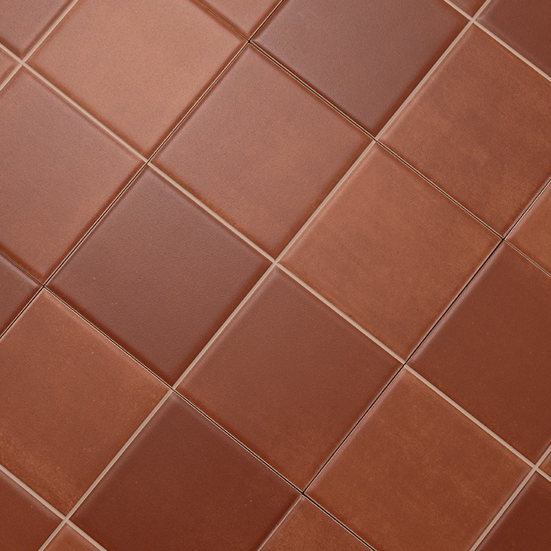 Rodebruine keramische tegels, diagonaal gelegd in raster met smalle beige voegen, afwisselend matte en lichtglanzende oppervlakken.