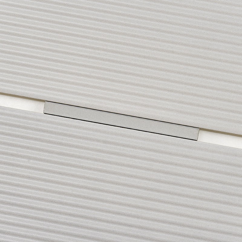 White striated tile with a rectangular metal groove embedded in the joint, bordered by a light shadow and a thin separation between two tiles.