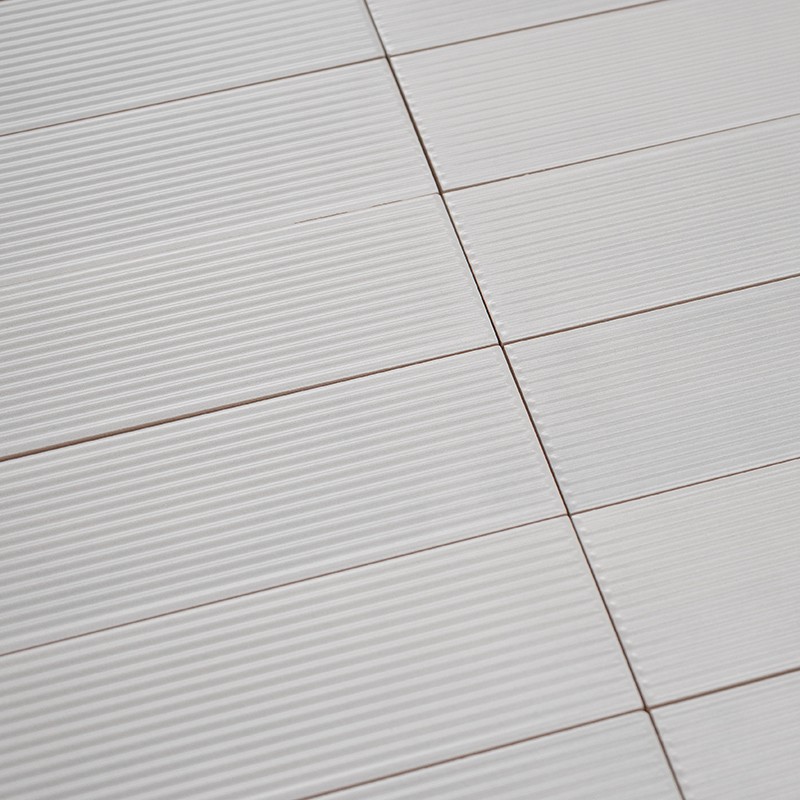 White rectangular tiles with a grooved texture, arranged in rows on a surface with thin joints; diagonal perspective view showing repeating pattern and soft shadows.