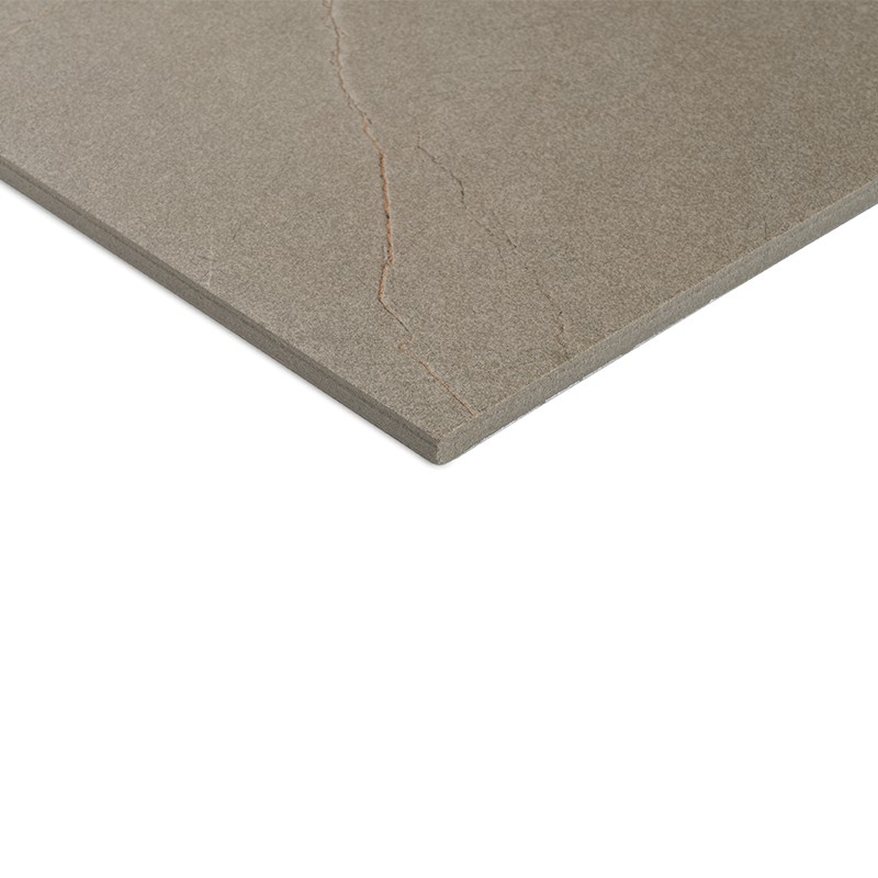 Azulejo rectangular gris-marrón con textura mate y una fina fisura; mostrado en esquina sobre fondo blanco liso, evidenciando grosor y borde biselado.
