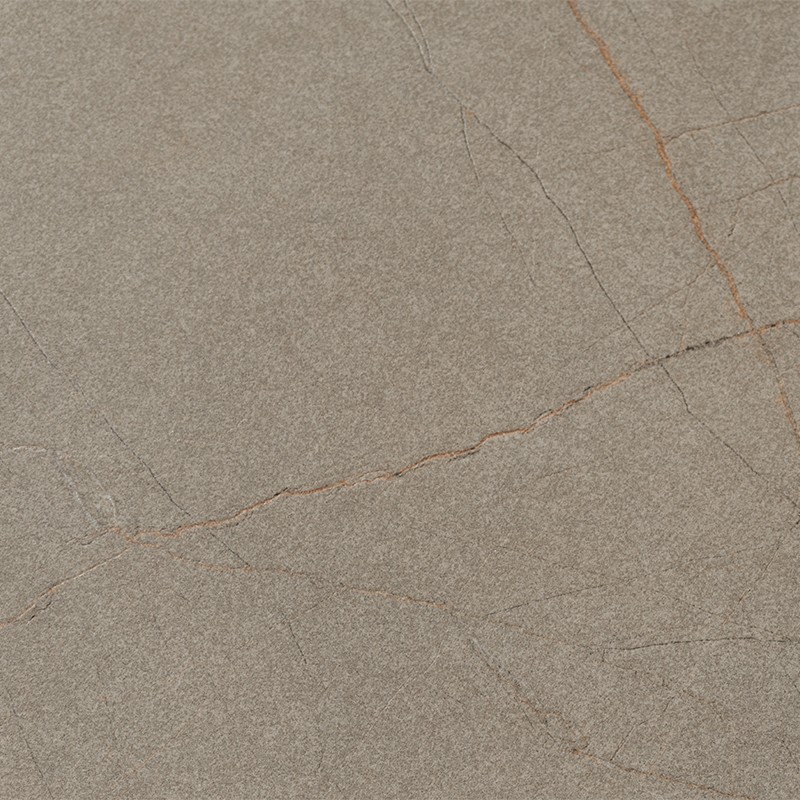 Azulejo gris-beige con textura mate, finas vetas y grietas marrón claro formando líneas diagonales; apariencia de piedra natural sobre superficie plana y uniforme.