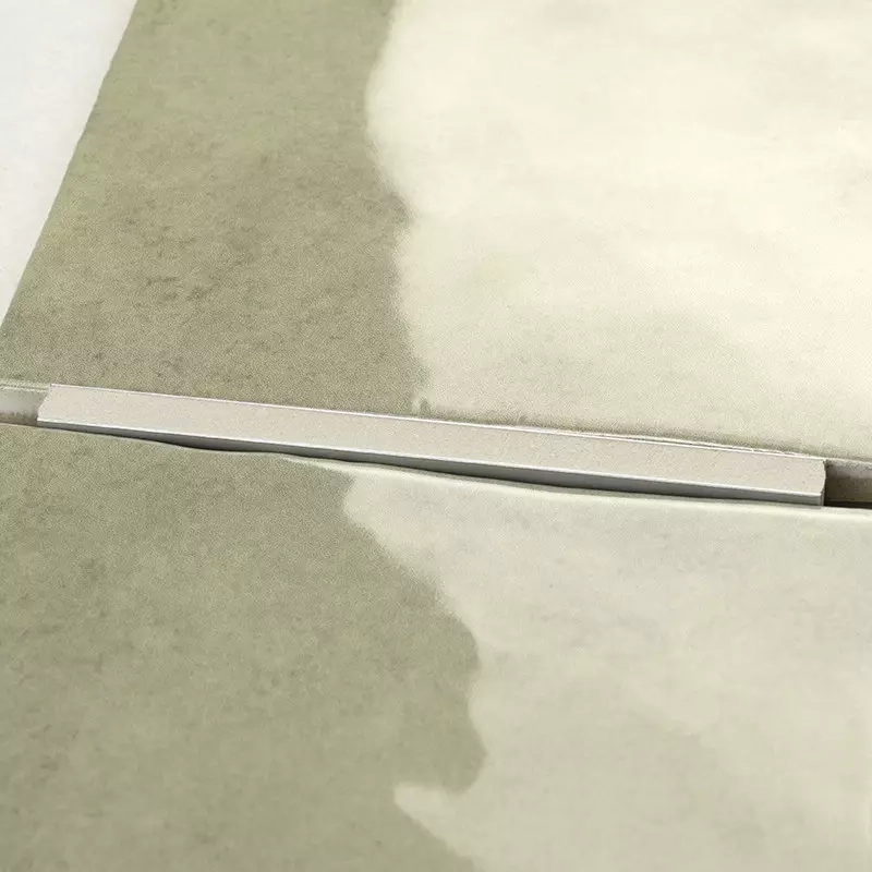Carrelage beige clair et kaki séparé par un joint fin et un profilé métallique étroit; surface partiellement ombrée avec dégradé irrégulier.