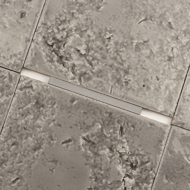Azulejo cerámico rugoso y moteado como foco; contexto: azulejos adyacentes con juntas rectas y separadores blancos formando un piso o pared.