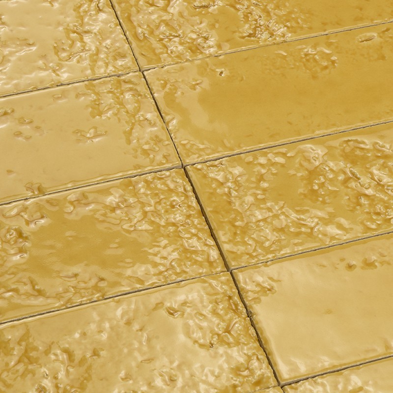 Yellow glazed tile with irregular texture; arranged in a grid, dark joints visible and shiny surface dotted with rough reliefs.
