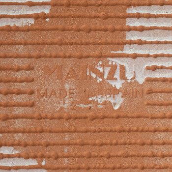 De terracotta tegel is voorzien van de tekst in reliëf: `MANZU MADE IN SPAIN`, met horizontale randen en wit gespikkelde gebiede