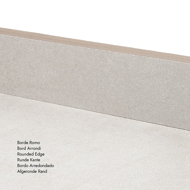 Fliese mit abgerundeter Kante, helle sandgraue Oberfläche; wandseitige Kante sichtbar, Bodenplatte im Vordergrund.  Text im Bild:  Borde Romo Bord Arrondi Rounded Edge Runde Kante Bordo Arredondado Afgeronde Rand