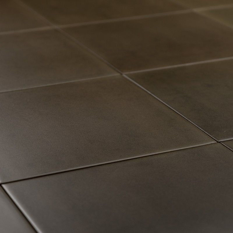 Carrelage sombre mat à grandes dalles carrées et joints fins, éclairage rasant créant légers reflets; sol intérieur uniforme et minimaliste.
