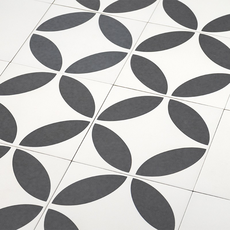 Azulejo blanco con patrón geométrico: óvalos oscuros que forman círculos entrelazados; varias baldosas contiguas crean un mosaico repetitivo sobre suelo liso.