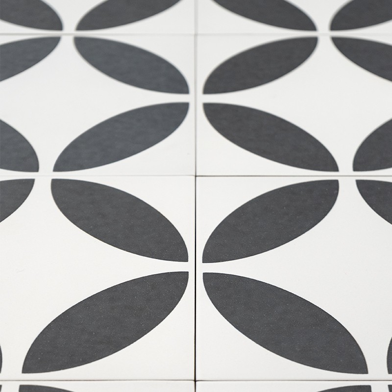 Azulejos brancos com padrão geométrico preto formando pétalas ovais repetidas; rejunte fino visível entre peças; composição modular monocromática possivelmente em piso ou parede.