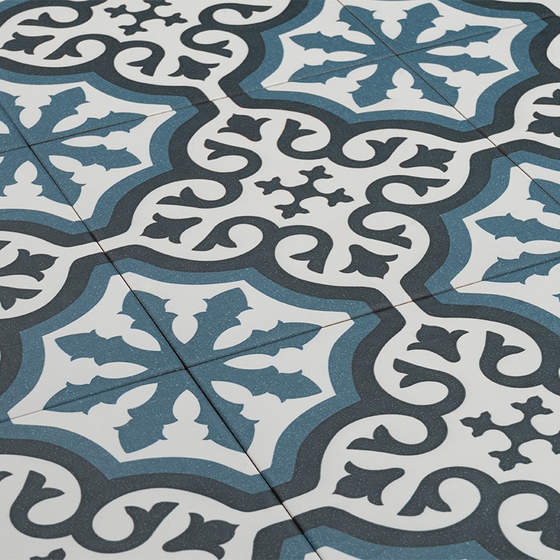Blaue, weiße und schwarze Bodenfliesen mit wiederholendem geometrischem Blumen- und Rankenmuster; vier Kacheln sichtbar, feine Fugen, leicht diagonal aufgenommen.