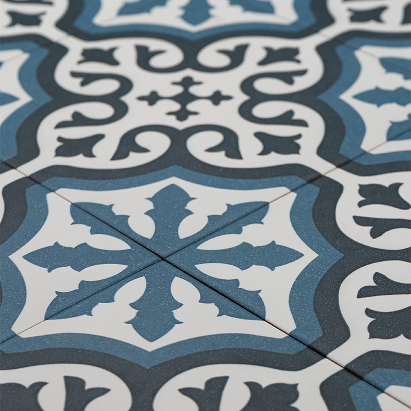 Square blue, white and grey ceramic tile with central arabesque motif; visible joints and a thin diagonal crack; identical adjacent tiles.