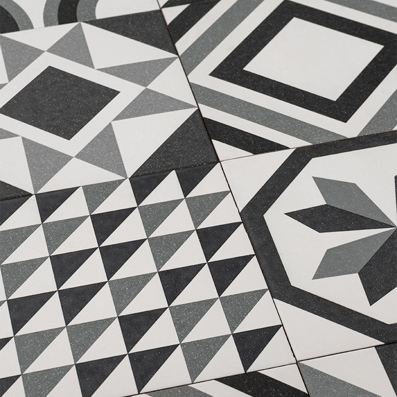 Carrelage céramique noir, blanc et gris à motifs géométriques variés (losanges, triangles, carrés concentriques, étoile), joints visibles, assemblé en surface plane.