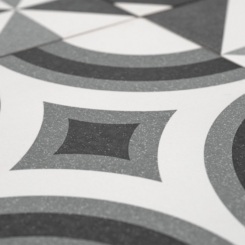 Carrelage géométrique: motifs concentriques et losanges arrondis en nuances de gris et noir sur fond blanc, surface légèrement granuleuse.