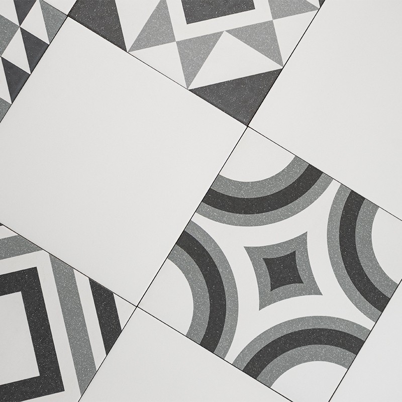 Carrelage géométrique : carreaux alternant unis et à motifs noir/gris (triangles, arcs concentriques et carrés), posés en diagonale sur un sol clair.
