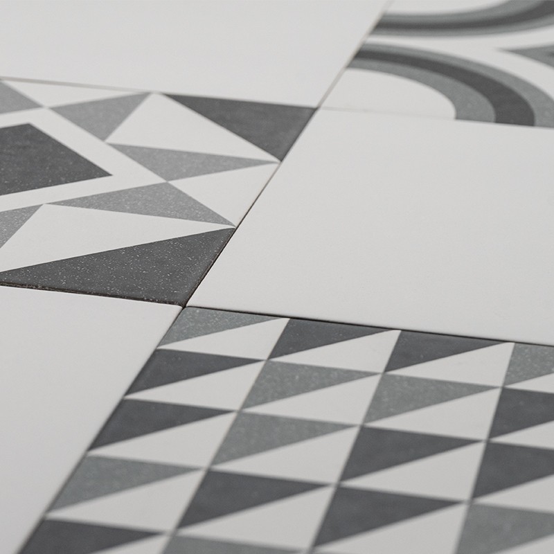 Carrelage composé de carreaux blancs et gris à motifs géométriques (triangles et arcs), posé à plat, vue rapprochée en perspective montrant jonctions et textures.