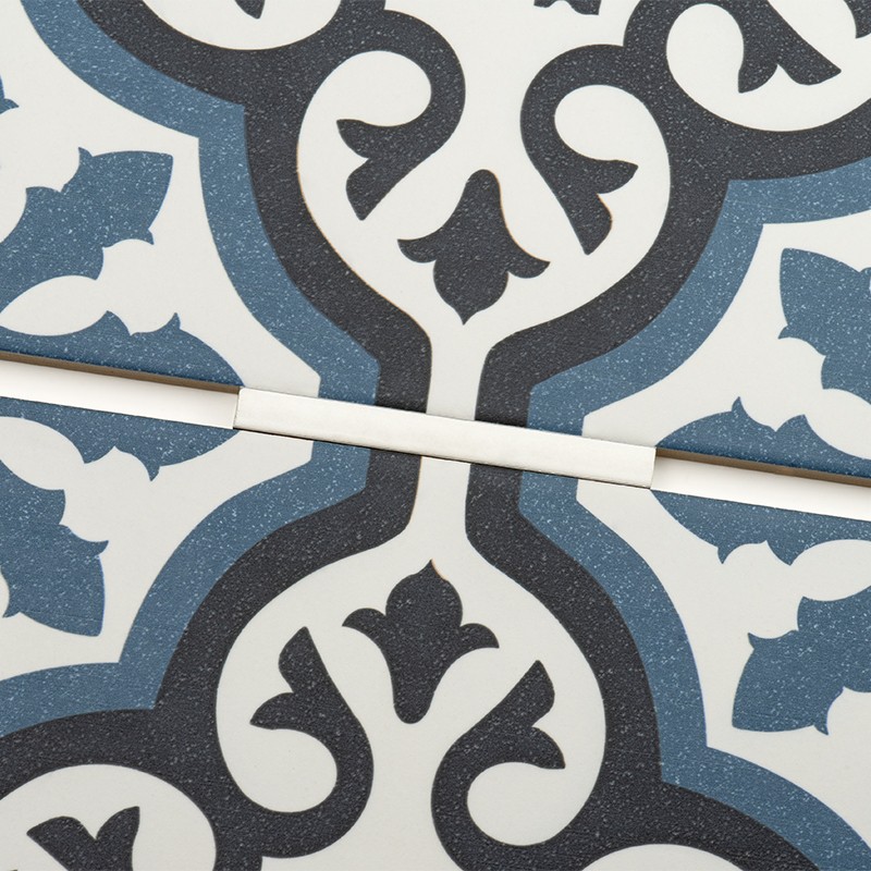 Ceramic tile with geometric and floral motifs in blue, black and white; centered white joint crosses the joint, separating two pieces of the cladding.
