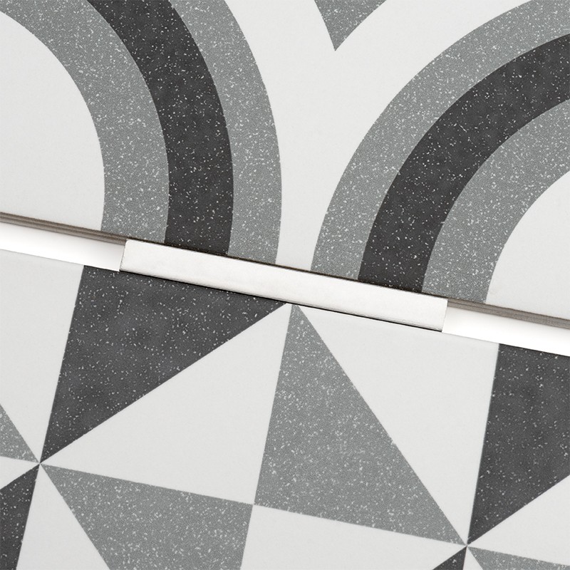 Carrelage aux motifs géométriques: arcs concentriques et triangles alternés en nuances de gris et blanc, finement granité, joints blancs séparant les carreaux.